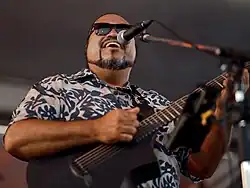 Eric Lee singing into a mic while playing guitar in Yokosuba, Japan, summer 2024