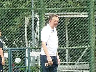 A man with short brown hair in a white shirt and black pants