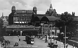Sepia-tone picture postcard with Victorian-era building with wagons, people and train cars out front; original caption in German: "Essen und Ruhr Neue Unterfuhring am Bahnhof" (?)