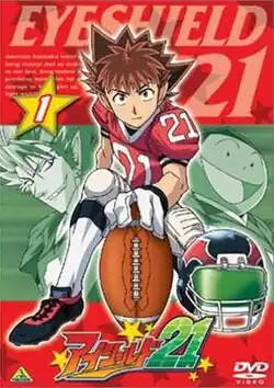 The cover depicts three young men. One of them is looking ahead and the other two behind him are with stern faces. The young man ahead has brown hair, a uniform that consists in a red T-shirt with the number twenty-one, a pair of white gloves, white pants, and football boots. He is holding an American football ball support on the floor and in front of him there is a helmet.