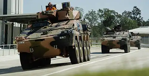 A single Boxer CRV and a pair of CRV-MPVs driving along the test track at Rheinmetall's Military Vehicle Centre of Excellence (MILVEHCOE) in 2019.