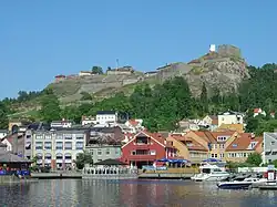 Modest buildings along the water's edge are guarded by a fortress on the hill above.