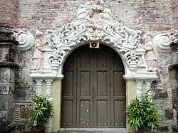 Ornate side portal, featuring pink reliefs of the Visitation at the top, and figures of Saint Zachary (vested as a kohen) and Saint Elizabeth to the sides