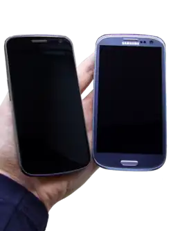 Photo of two phones turned off held next to each other with warm yellow ambience lightning. The phones are rested on a person's hand.