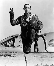 A man standing in the cockpit of an aircraft that is on the ground.