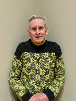 Crowley, an elderly white man with short grey hair, wearing a knitted jumper with a bright green chequered design.