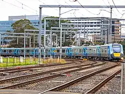 A long train arriving into Dandenong station, with 4 tracks, signalling, and electrical equipment shown