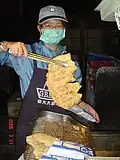 Man picking up fried chicken cutlet with tongs to sell; March 2006