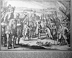 A man wearing a large hat receives an other man, both being surrounded by a large crowd of armed people