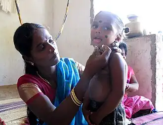 A Tamil woman applying kajal on her toddler son in India