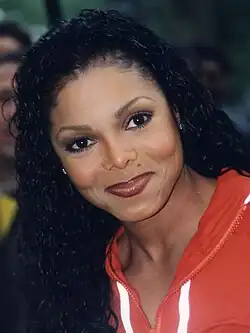 Janet Jackson smiling for the camera in an orange jacket.