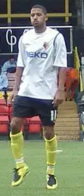 Man wearing white T-shirt, black shorts and yellow socks, standing on a pitch