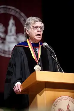 Levine stands at a lectern wearing academic robes and a medal