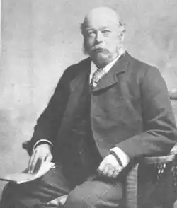 A black and white portrait of a man in a suit sitting in a chair.