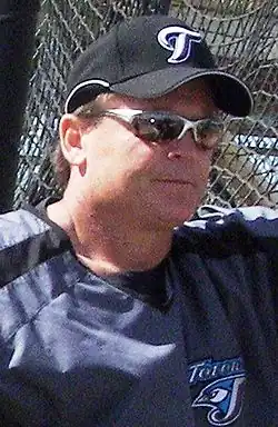 Man in sunglasses and baseball uniform leaning against a fence