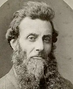 Long-nosed man with serious expression, long chinstrap beard and upswept hair