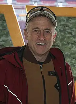 Photo of a man smiling while wearing a baseball cap and red jacket.