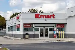 One-story grey shopping building with "Kmart" signage over the door. The store takes up a corner in the shopping center.
