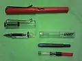 Lamy Safari (top) in red and Vista (bottom) fountain pens. Under the Lamy Vista transparent demonstrator pen a Lamy T10 ink cartridge and a Lamy Z 24 piston operated converter for using bottled fountain pen ink.