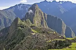 Stone ruins of Machu Picchu set on a mountain ridge, with steep green peaks in the background.