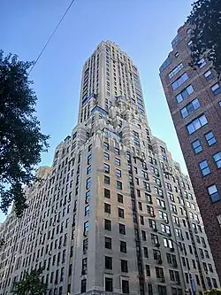The hotel tower as seen from 76th Street and Madison Avenue. The tower stories are set back from the base, and the facade is made of beige brick, with rectangular windows. A red brick building is visible at right.