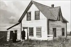 Two men in cassocks in front of a house.