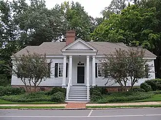 Photo of a one-story home painted white with black shutters and a porch with four pillars.