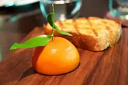 A mousse in the shape of a half mandarin orange, including a leafy stem.