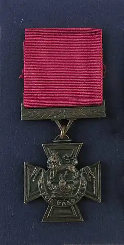 a photograph of a bronze medal with a crimson ribbon attached