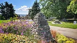 Cairn made of stones and mortar with a bronze plaque, surrounded by gardens in a city park