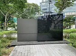 The memorial, the black and grey structure at the centre amidst greenery at Dhoby Ghaut Green