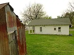 "A white, wooden house with a greenish roof in the middle of a green lawn."