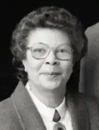 Head shot of Nilon, who has shirt curly hair and is wearing a dark jacket and a white shirt