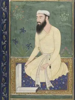A color photograph of a miniature painting. The painting depicts a bearded man seated on a carpet
