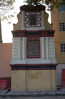 Picture of a three-story monument. From bottom to top, the foundation is a sculpted wall; the second story depicts the Archangel Gabriel announcing to the Virgin Mary that she would conceive and become the mother of Jesus. The top story features an image of Our Lady of Guadalupe.