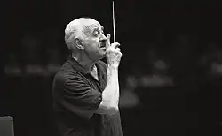 A black-and white image of a man wearing a suit jacket and shirt, with his arms raised