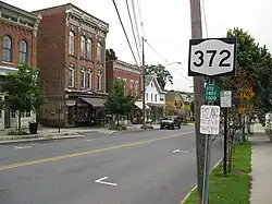 A NY 372 shield attached a post near a telephone pole in the middle of a village