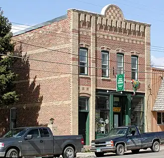 A small, two-story brick building directly fronting a street with parked trucks