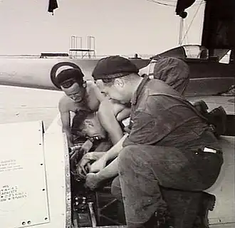 Three men in overalls working on an aircraft engine