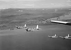 Black and white photo of four single-engined military monoplanes flying in formation near a coastline
