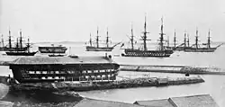 The Grassy Bay anchorage seen from the Royal Naval Dockyard in Bermuda in 1865, with the hulk of HMS Medway tied to the wharf and another hulk anchored at Grassy Bay.