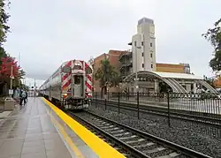 A train at a railroad station with a parking garage behind