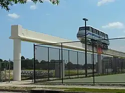 A white and blue monorail looking vehicle sitting on metal track on a concrete beam. The photo is grainy and washed out.