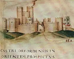 A group of connected towers surrounded by a wall and more tower, with uneven ground in front.