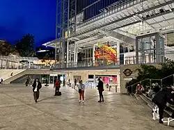 A wide entrance behind an incline, surrounded by an Underground roundel and a sign pointing to the entrance for the Bakerloo line. The surfaces are finished in a modern, high-end manner.