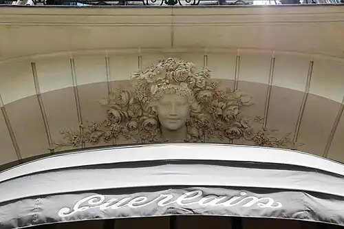 Beaux Arts mascaron with a multitude of flowers around it, above a window of the parfumery of Jacques and Pierre Guerlain, (Avenue des Champs-Élysées no. 68), Paris, designed by architect Charles-Frédéric Méwès and decorated by Bérard Christian, 1912[50]