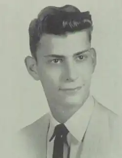 A black-and-white bust-length photo of a young white man in a light-colored suit and tie