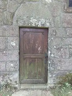 A wooden door on a granite wall. The top of the door is inscribed "ES YGLESIA DE REFUGIO".