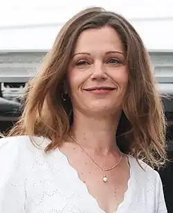 Headshot of a woman with light brown hair, wearing a white dress, and smiling as she boards a plane