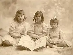Three little girls sitting cross-legged with a large book in front of them.